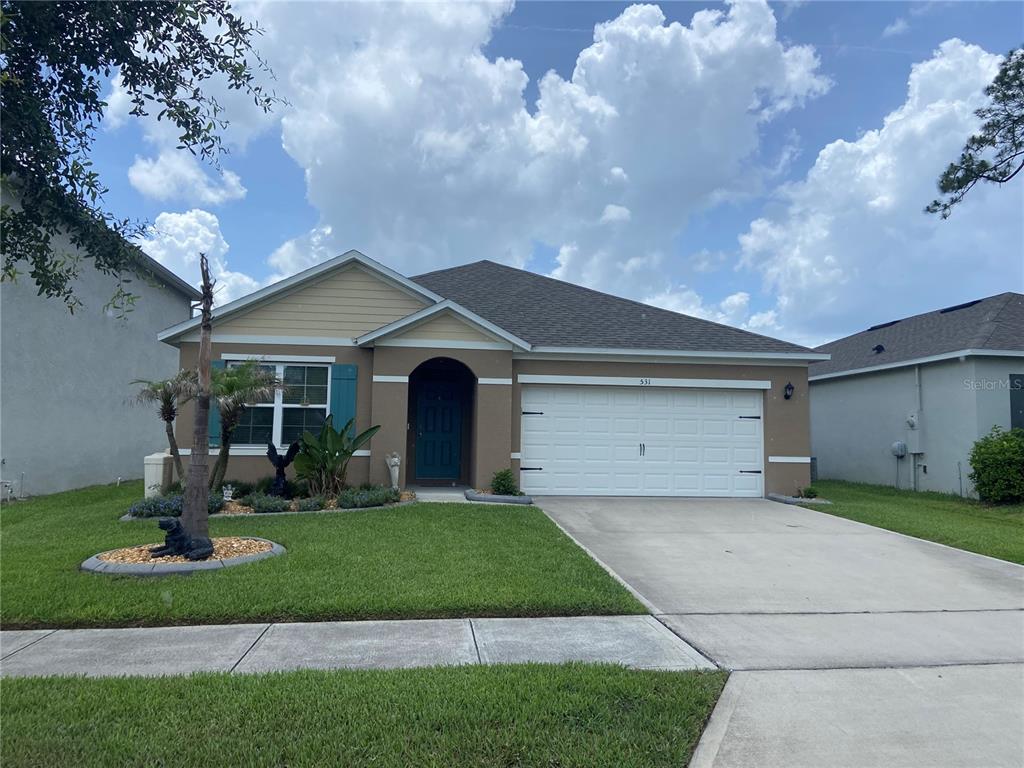 A single-story house with a tan stucco exterior, a two-car garage, and a front lawn — 531 EMILY GLEN STREET, DELAND, FL