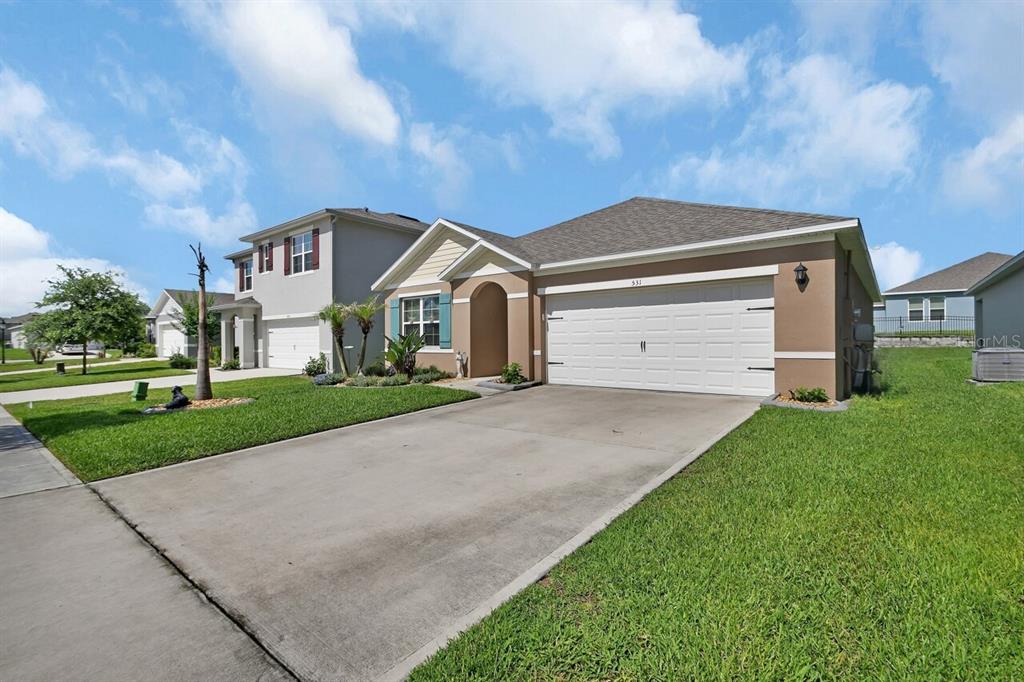 A single-story suburban house with a tan exterior, a two-car garage, and a concrete driveway — 531 EMILY GLEN STREET, DELAND, FL