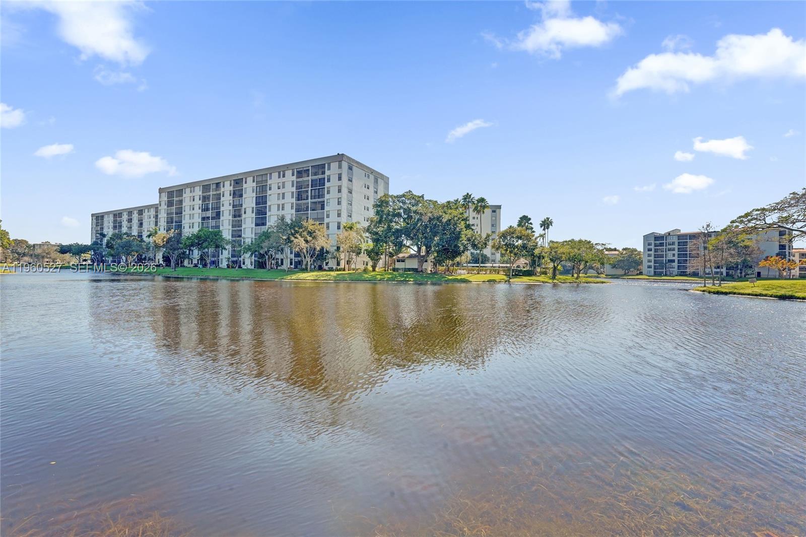 A large apartment building stands behind a calm lake surrounded by green landscaping — 2228 N Cypress Bend Dr # 103, Pompano Beach FL 33069, POMPANO BEACH, FL