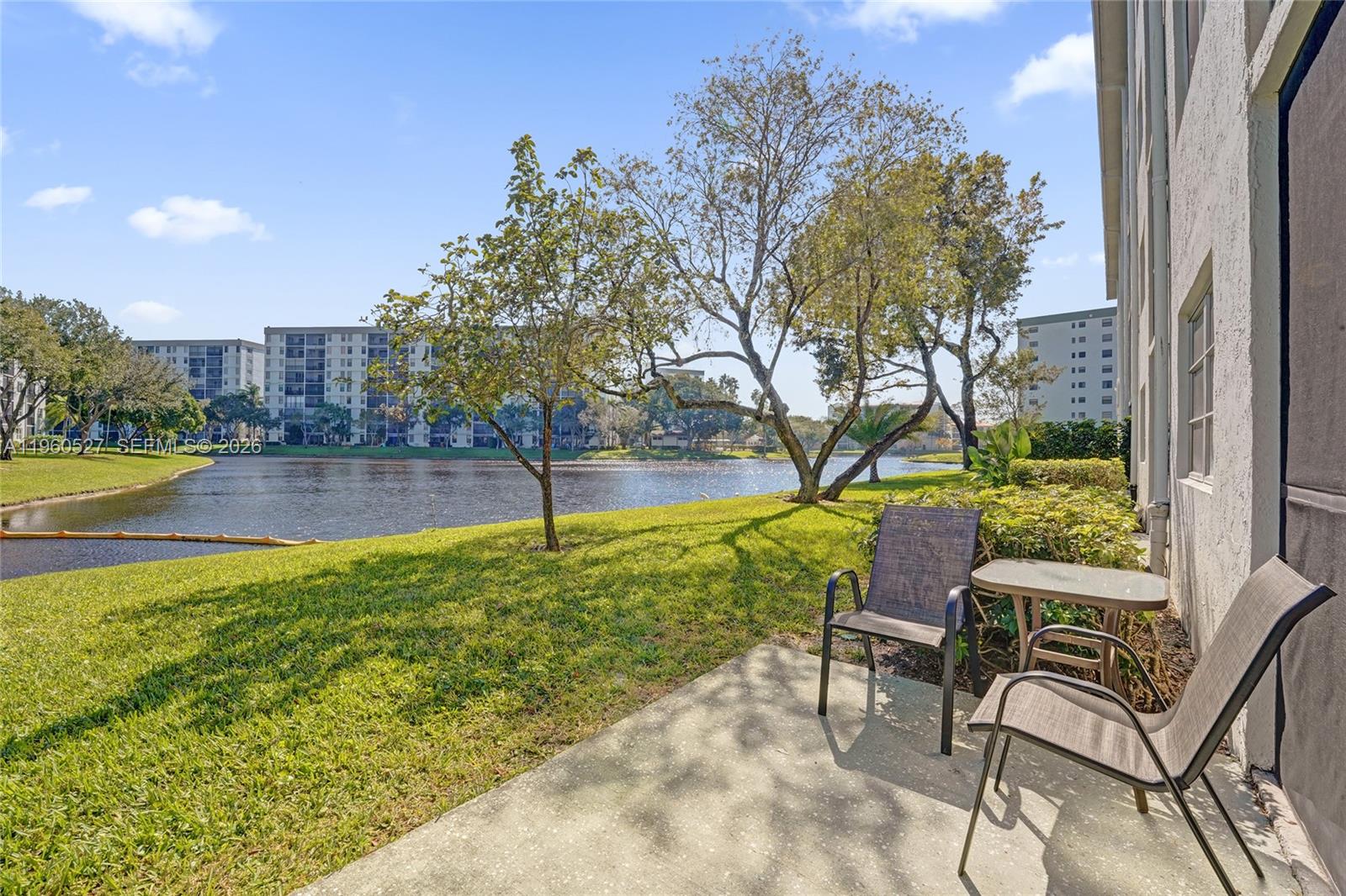 A concrete patio with outdoor furniture overlooks a grassy lawn and a lake — 2228 N Cypress Bend Dr # 103, Pompano Beach FL 33069, POMPANO BEACH, FL