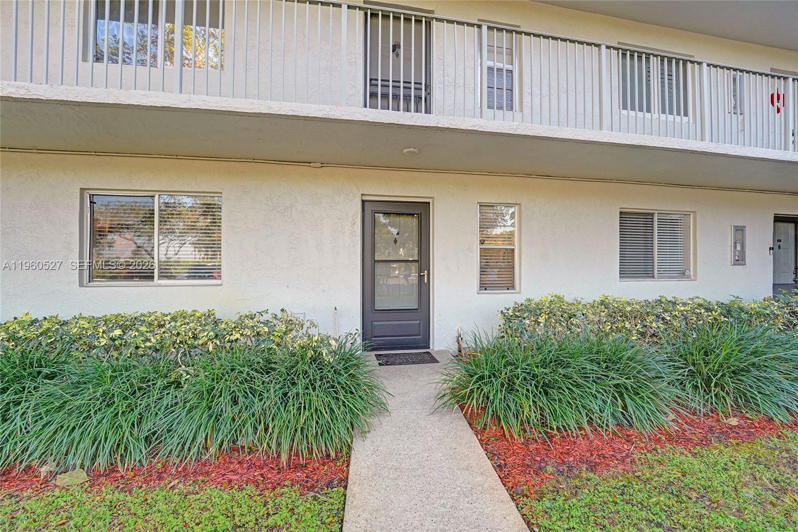 The exterior of a two-story apartment building features a ground-level entrance with landscaping — 2228 N Cypress Bend Dr # 103, Pompano Beach FL 33069, POMPANO BEACH, FL