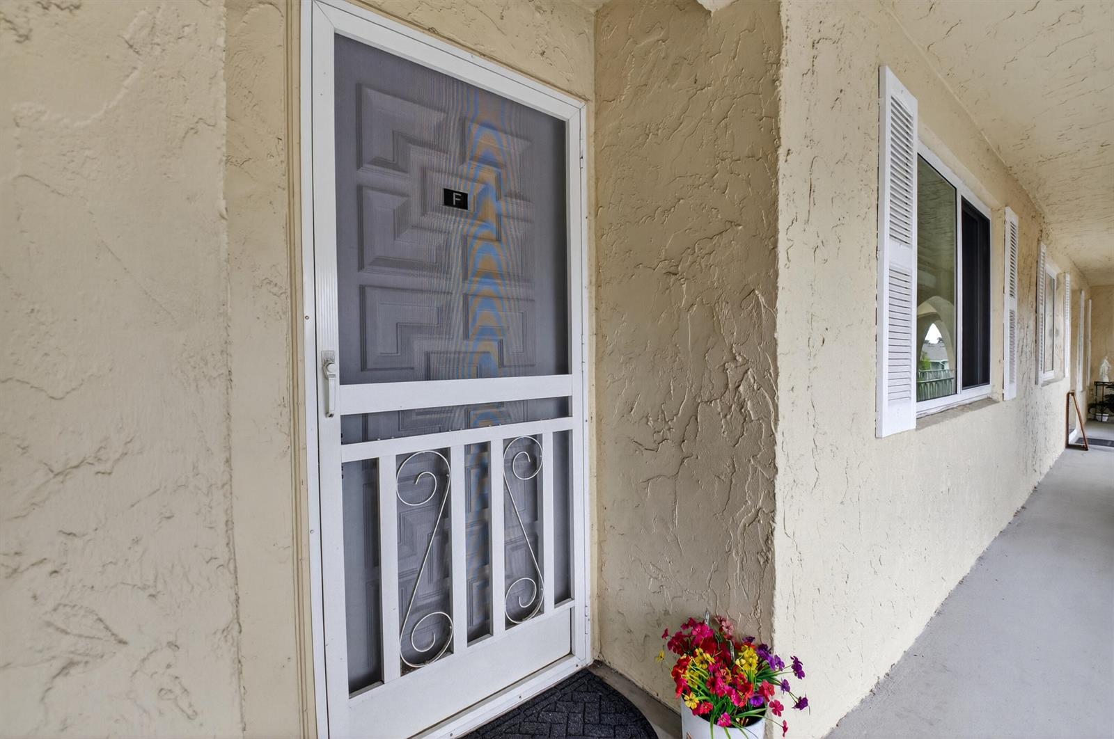 A white screen door with a letter F label leads to a tan stucco building exterior — 13767 Flora Place # F, Delray Beach FL 33484, DELRAY BEACH, FL