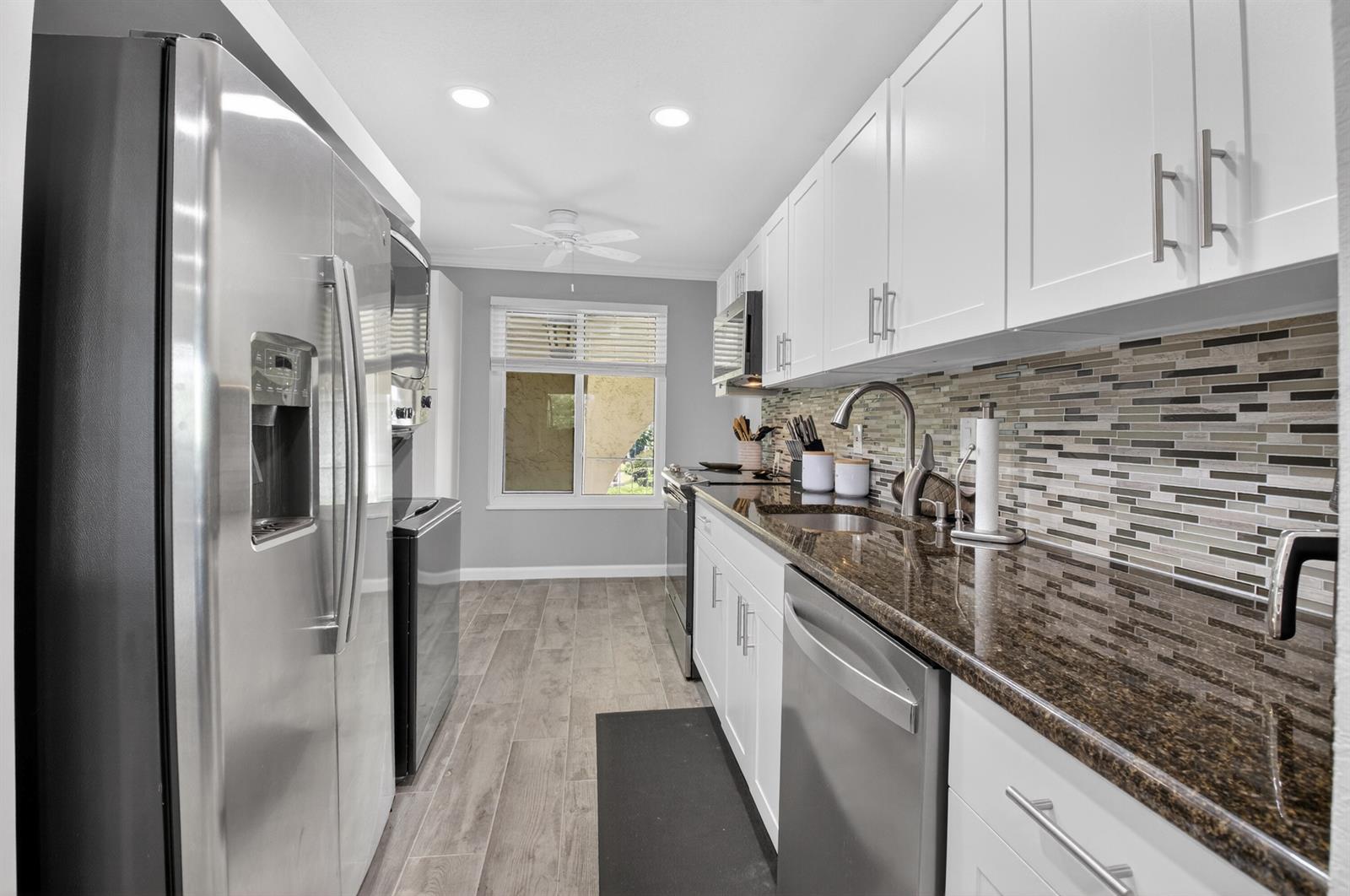 A galley kitchen features white cabinets, dark granite countertops, stainless steel appliances, and tile flooring — 13767 Flora Place # F, Delray Beach FL 33484, DELRAY BEACH, FL