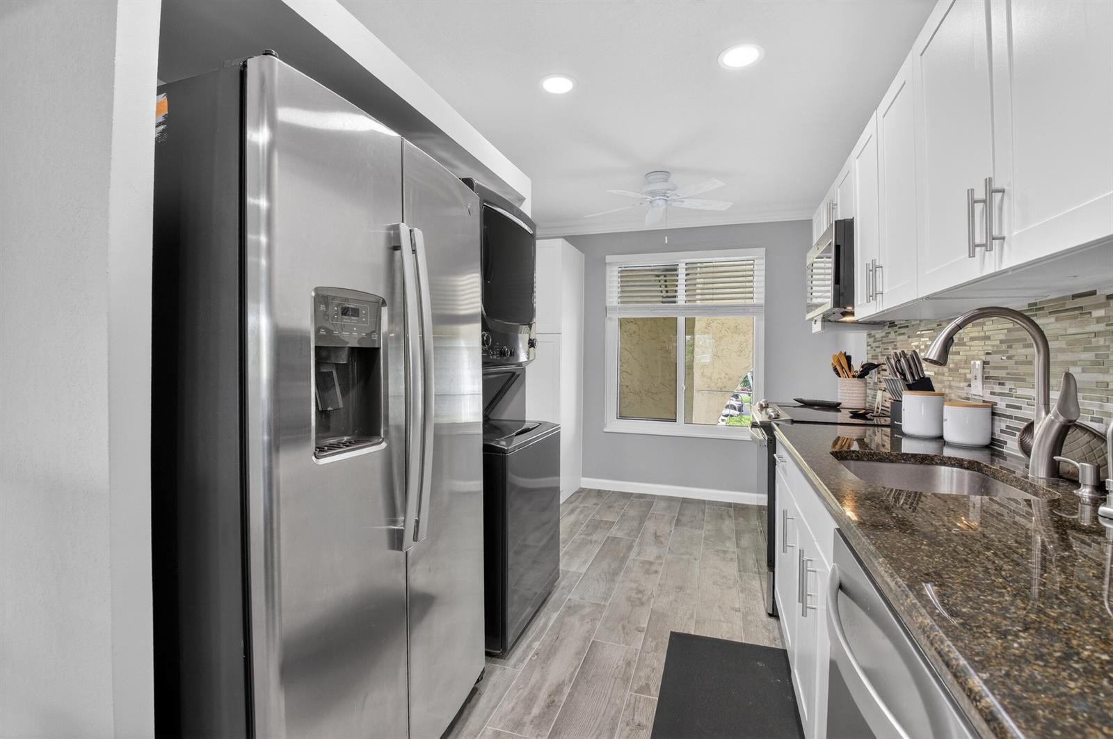 A galley kitchen features stainless steel appliances, white cabinets, dark granite countertops, and wood-look flooring — 13767 Flora Place # F, Delray Beach FL 33484, DELRAY BEACH, FL