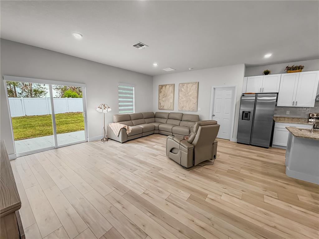 A living room with light wood floors, a grey sectional, and a sliding glass door — 13340 SW 49TH AVENUE, OCALA, FL