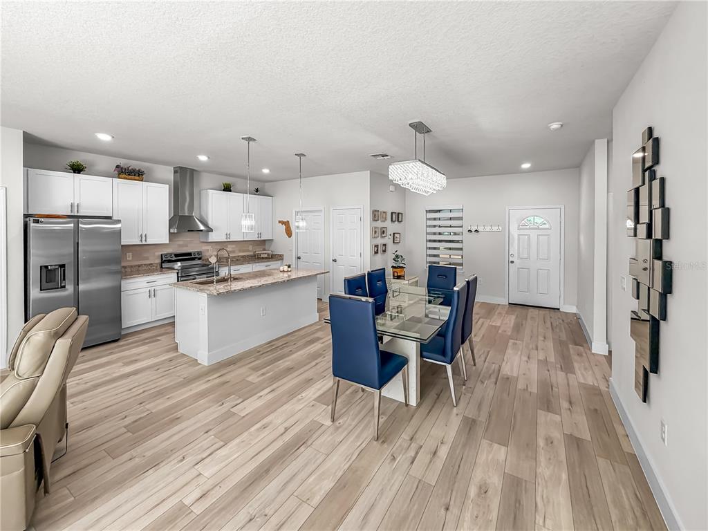 An open-concept kitchen and dining area features white cabinetry, a granite island, and blue chairs — 13340 SW 49TH AVENUE, OCALA, FL