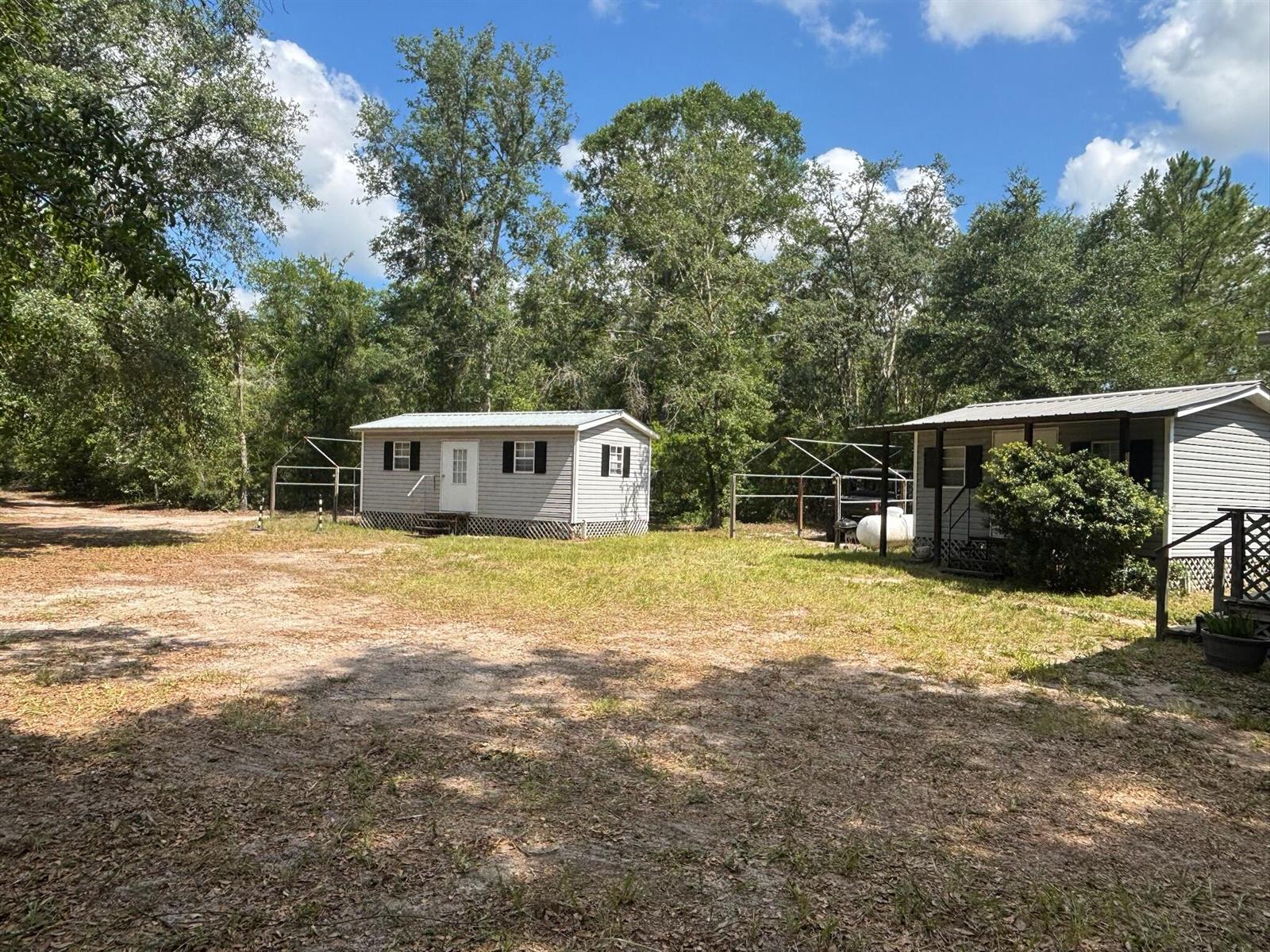 Two small, light-gray siding structures sit on a grassy lot surrounded by trees — 423 NW Bright Lake Court, FL 32096, FL