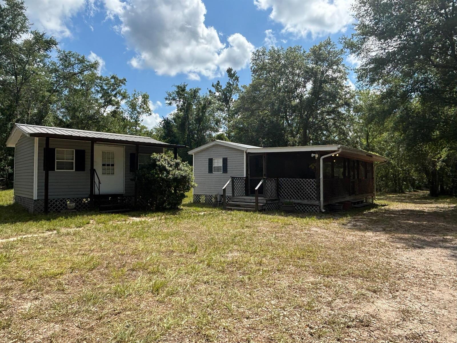 Two small, gray-sided houses with metal roofs sit on a grassy, wooded lot — 423 NW Bright Lake Court, FL 32096, FL