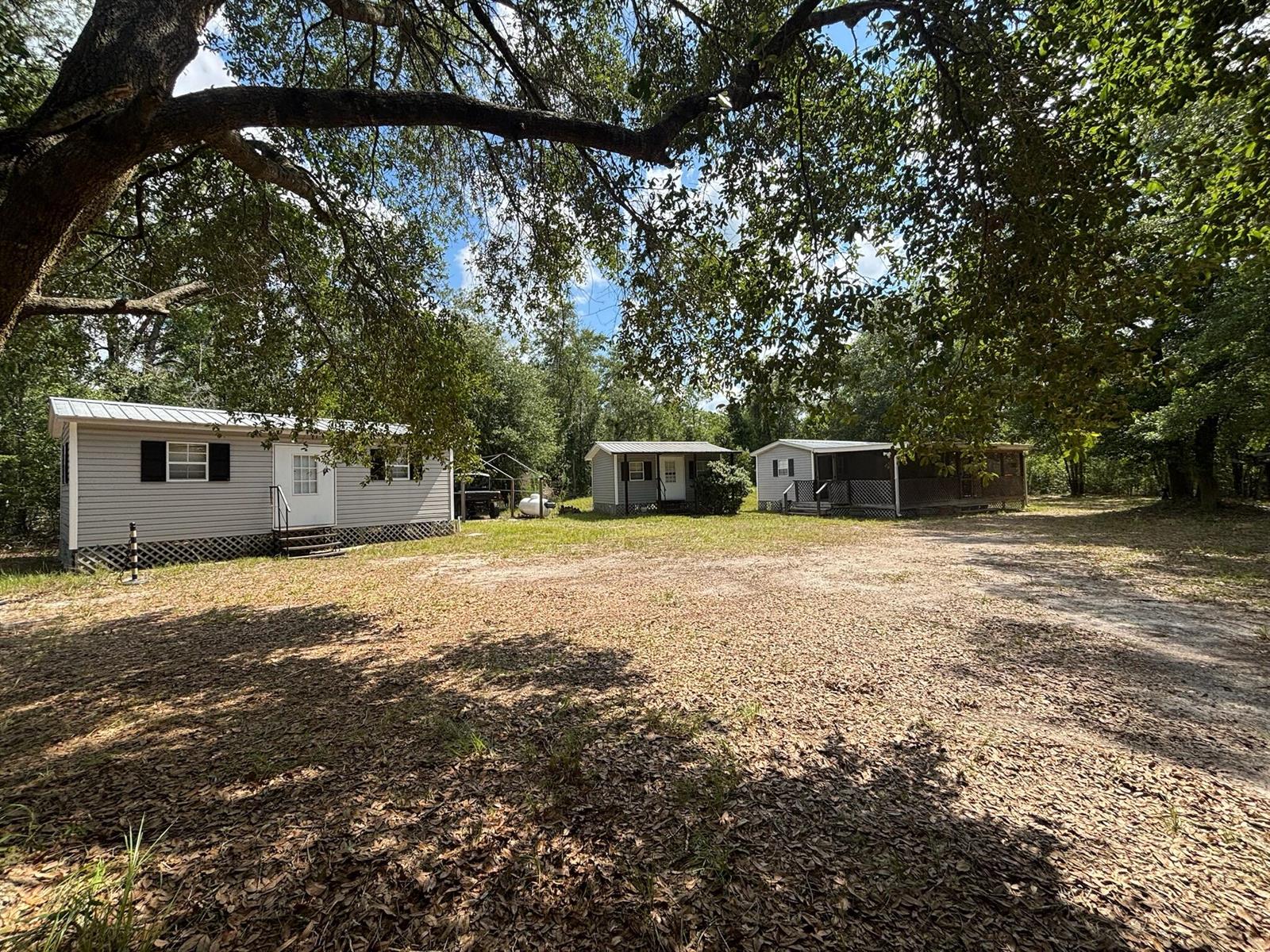 Three small, light-colored modular homes sit on a large, leaf-covered dirt lot under trees — 423 NW Bright Lake Court, FL 32096, FL