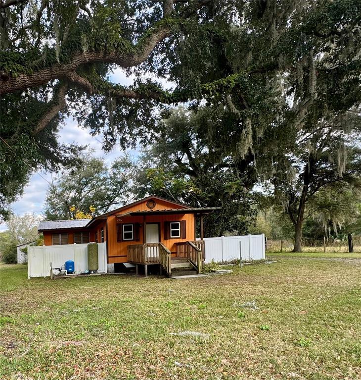 A small orange house with a wooden porch sits under large trees behind a fence — 1981 CR 615B, BUSHNELL, FL