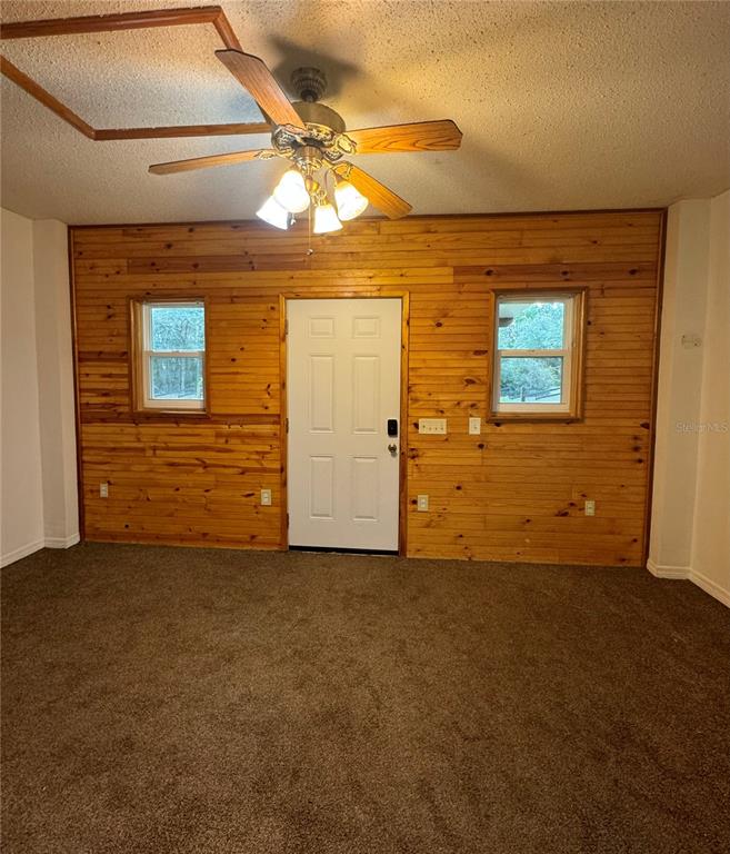 A room with brown carpet, wood-paneled walls, a ceiling fan, and a central exterior door — 1981 CR 615B, BUSHNELL, FL