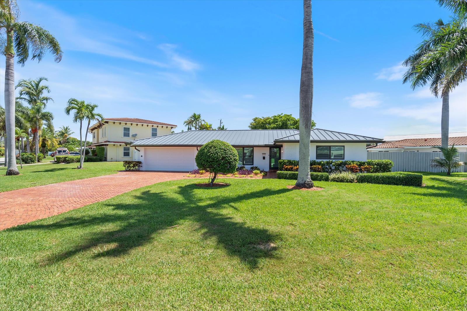 A single-story white house with a metal roof and a brick driveway sits on grass — 4410 NE 24th Avenue, Lighthouse Point FL 33064, LIGHTHOUSE POINT, FL