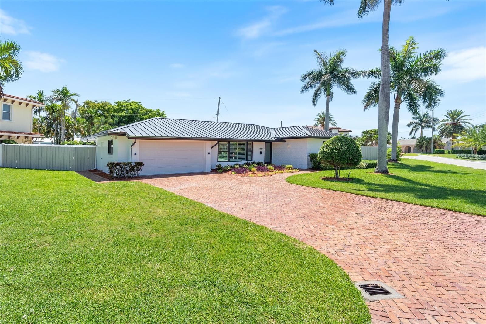 A single-story house with a white exterior, dark metal roof, and a brick driveway — 4410 NE 24th Avenue, Lighthouse Point FL 33064, LIGHTHOUSE POINT, FL