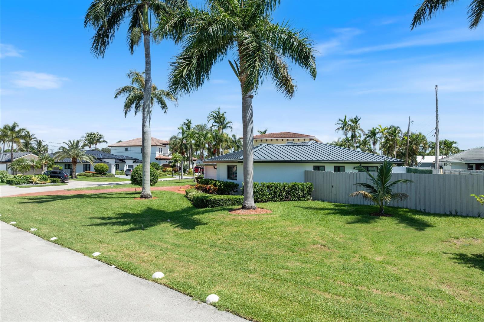 A white house with a dark metal roof sits on a grassy lot with palm trees — 4410 NE 24th Avenue, Lighthouse Point FL 33064, LIGHTHOUSE POINT, FL
