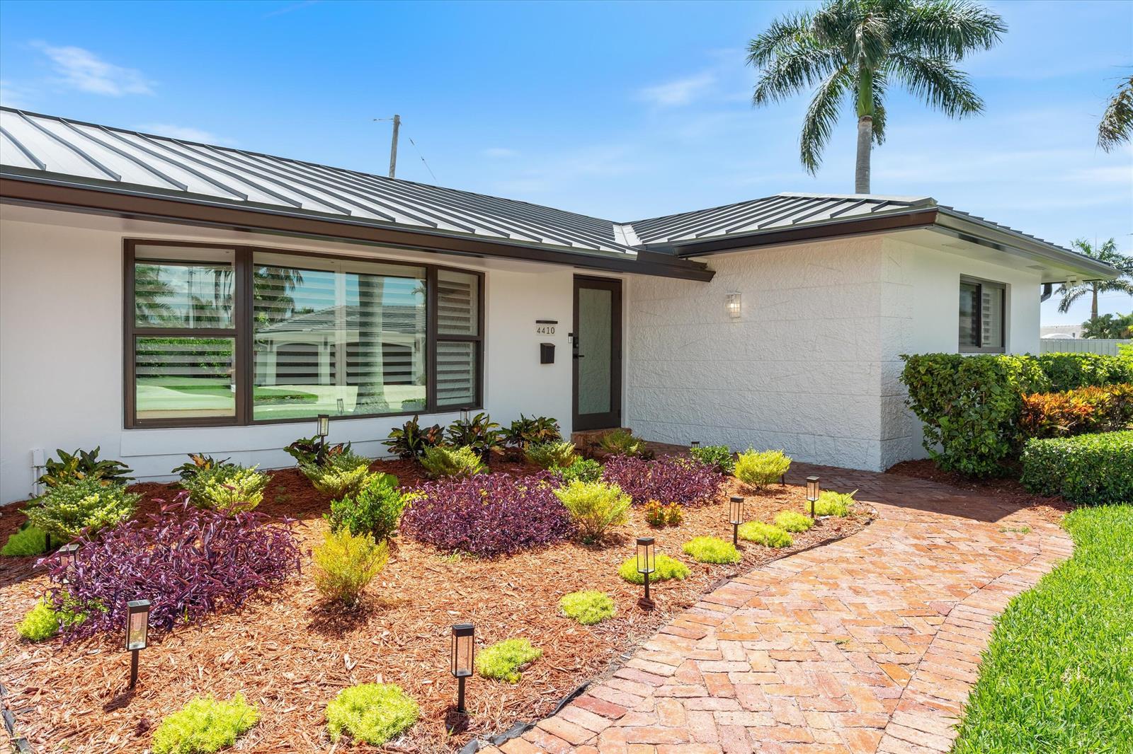 A single-story house with a white exterior, metal roof, and a brick walkway — 4410 NE 24th Avenue, Lighthouse Point FL 33064, LIGHTHOUSE POINT, FL