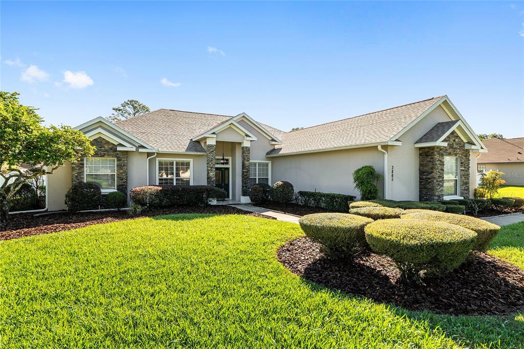 A single-story house with a beige stucco exterior, stone accents, and a manicured front lawn — 3865 SE 52ND AVENUE, OCALA, FL