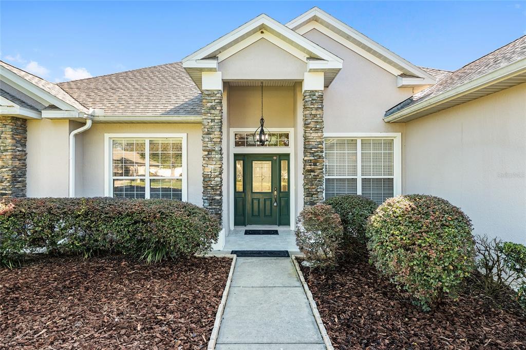 The exterior of a house features a green front door, stone columns, and landscaping — 3865 SE 52ND AVENUE, OCALA, FL