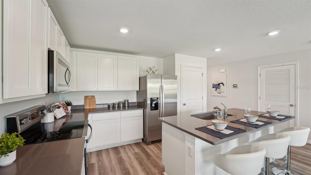 A modern kitchen features white cabinets, stainless steel appliances, and a central island with seating — 11019 NW 167TH TERRACE, ALACHUA, FL