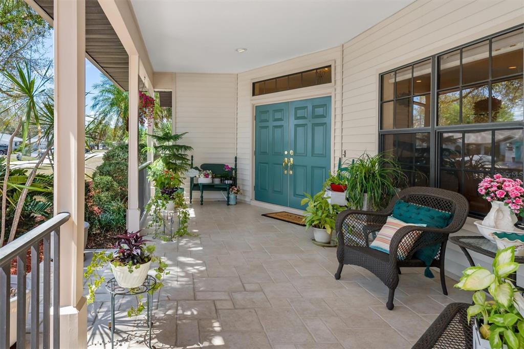 A covered front porch features tiled flooring, a teal double door, and various potted plants — 18412 MEYER AVENUE, PORT CHARLOTTE, FL