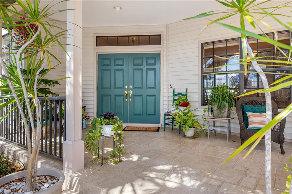 A covered front porch features a teal double door, tiled flooring, and various potted plants — 18412 MEYER AVENUE, PORT CHARLOTTE, FL
