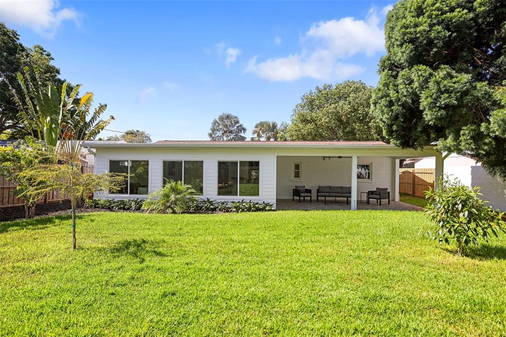 The exterior of a white house features a covered patio and a large grassy backyard — 4229 7TH AVENUE N, ST PETERSBURG, FL