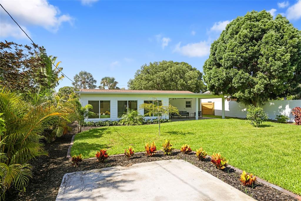 A backyard view of a white house with a covered patio and a grassy lawn — 4229 7TH AVENUE N, ST PETERSBURG, FL