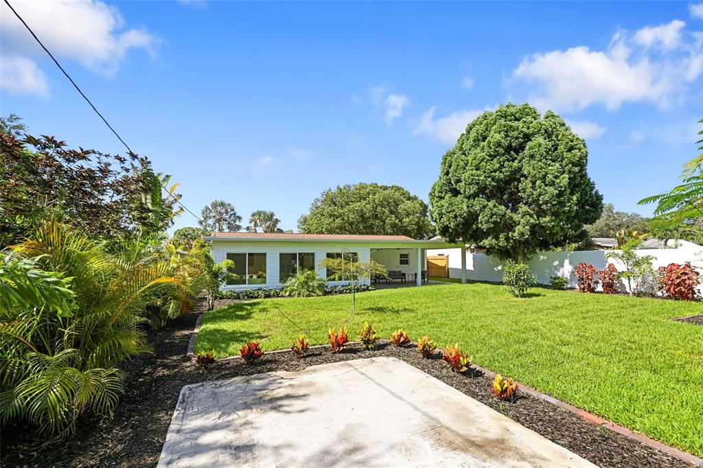 A white house with a covered patio overlooks a grassy backyard with tropical landscaping — 4229 7TH AVENUE N, ST PETERSBURG, FL