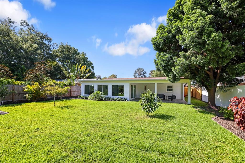A white house with a covered patio sits in a large, grassy backyard with trees — 4229 7TH AVENUE N, ST PETERSBURG, FL