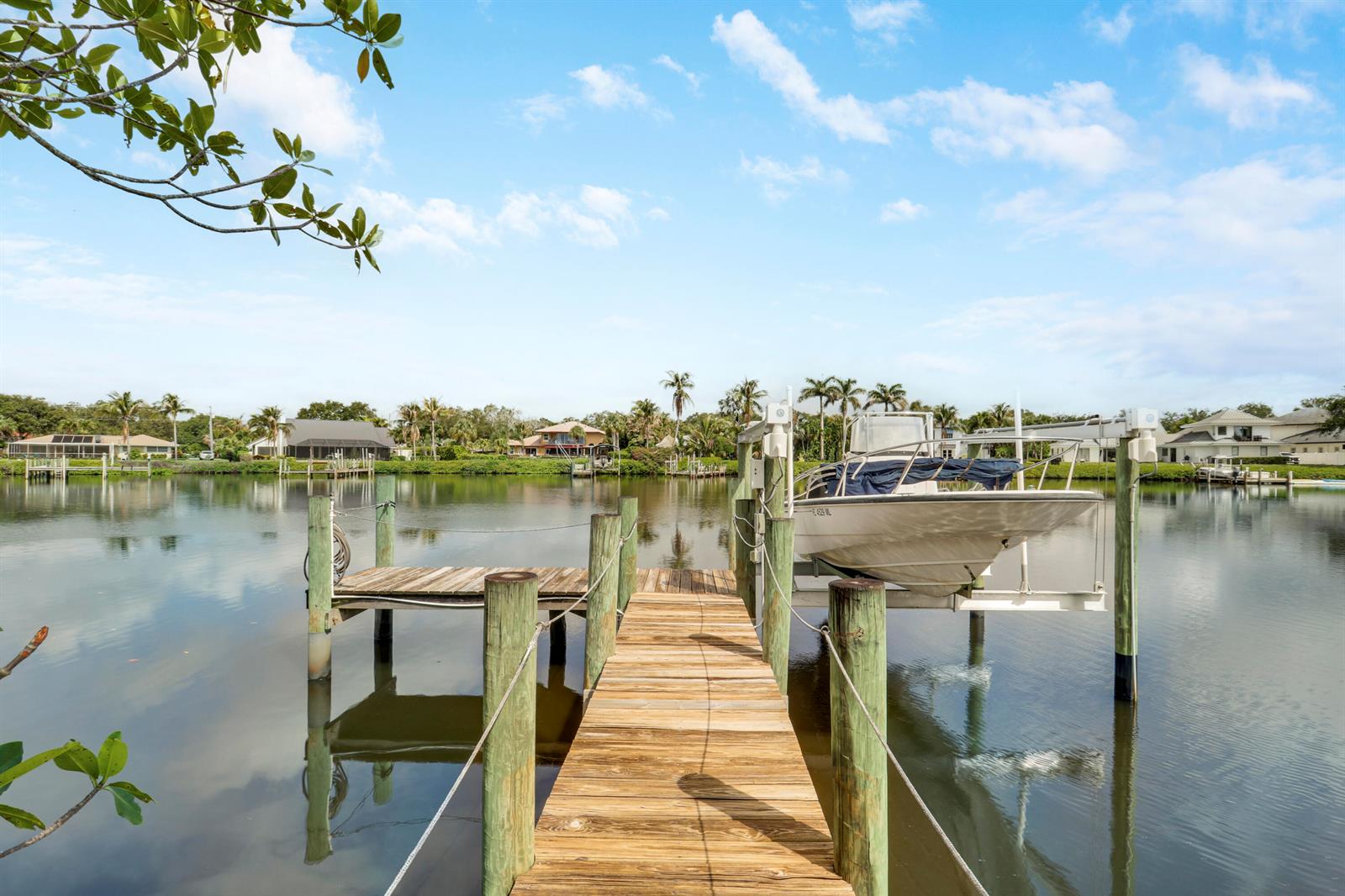 A wooden dock extends into a calm canal with a boat on a lift — 18791 SE River Ridge Road, Jupiter FL 33469, JUPITER, FL