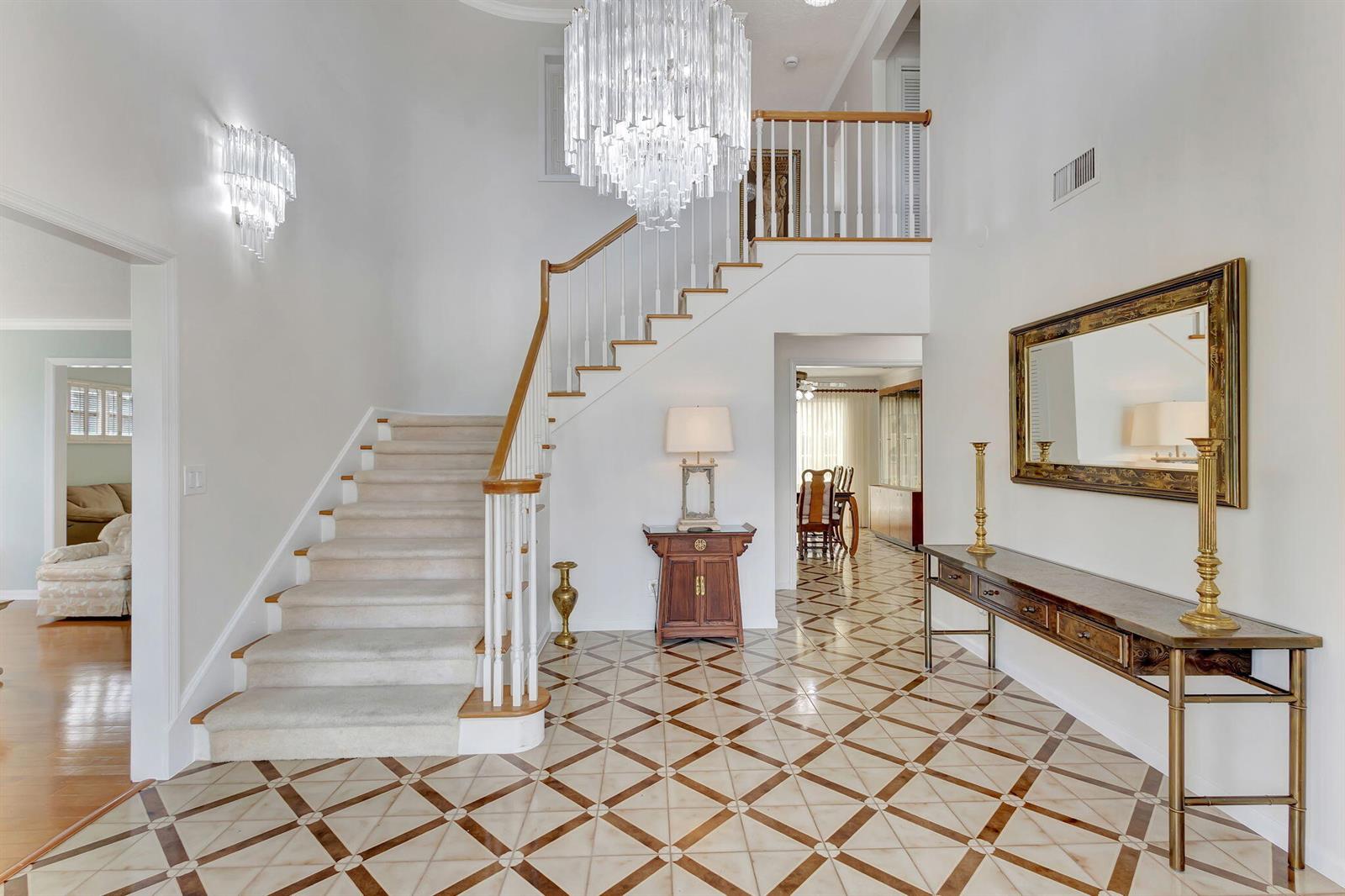 A grand foyer features a carpeted staircase, a crystal chandelier, and patterned tile flooring — 1141 Pine Point Road, West Palm Beach FL 33404, WEST PALM BEACH, FL