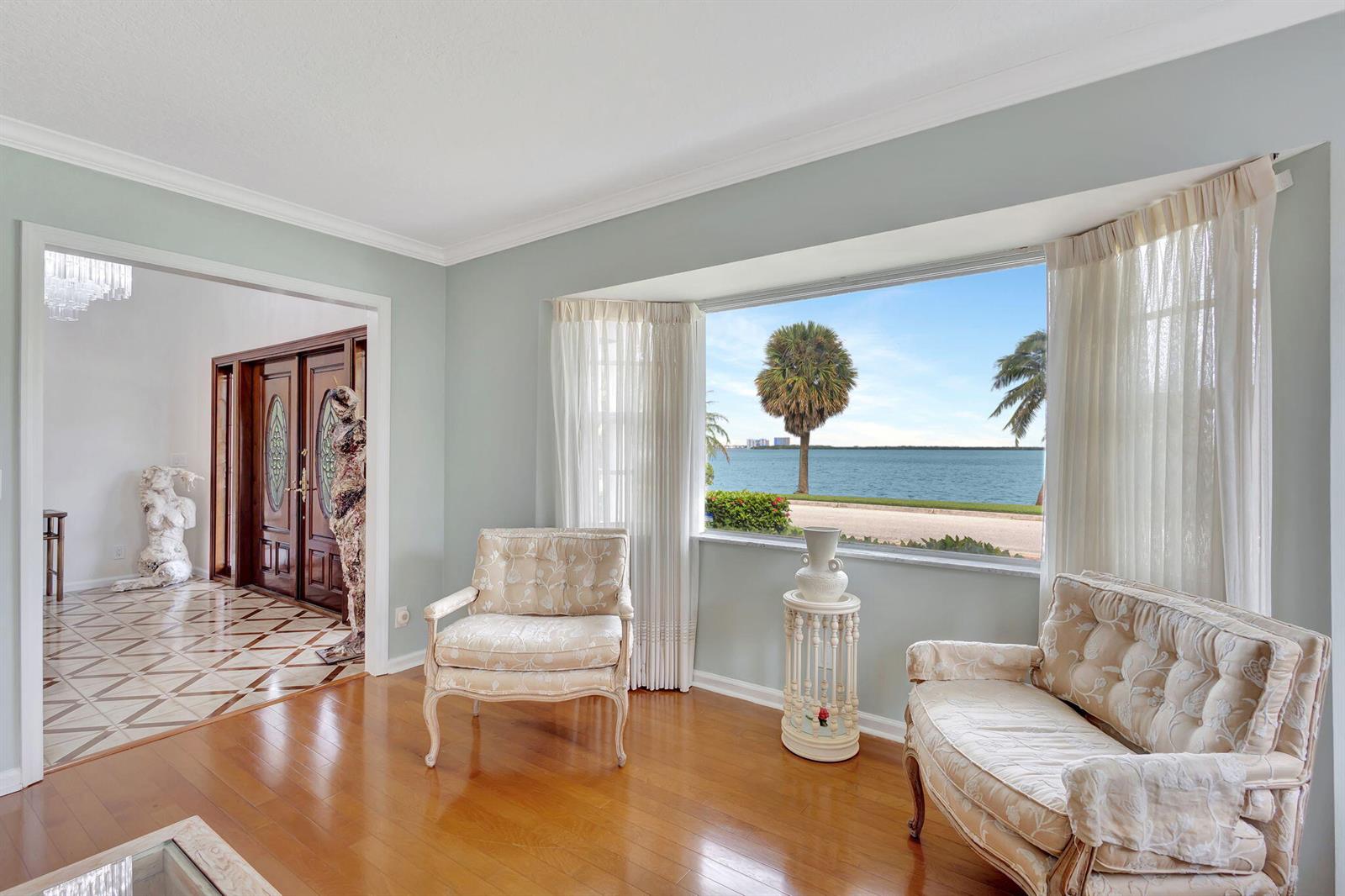 A living room with light blue walls, hardwood floors, and a large window overlooking water — 1141 Pine Point Road, West Palm Beach FL 33404, WEST PALM BEACH, FL