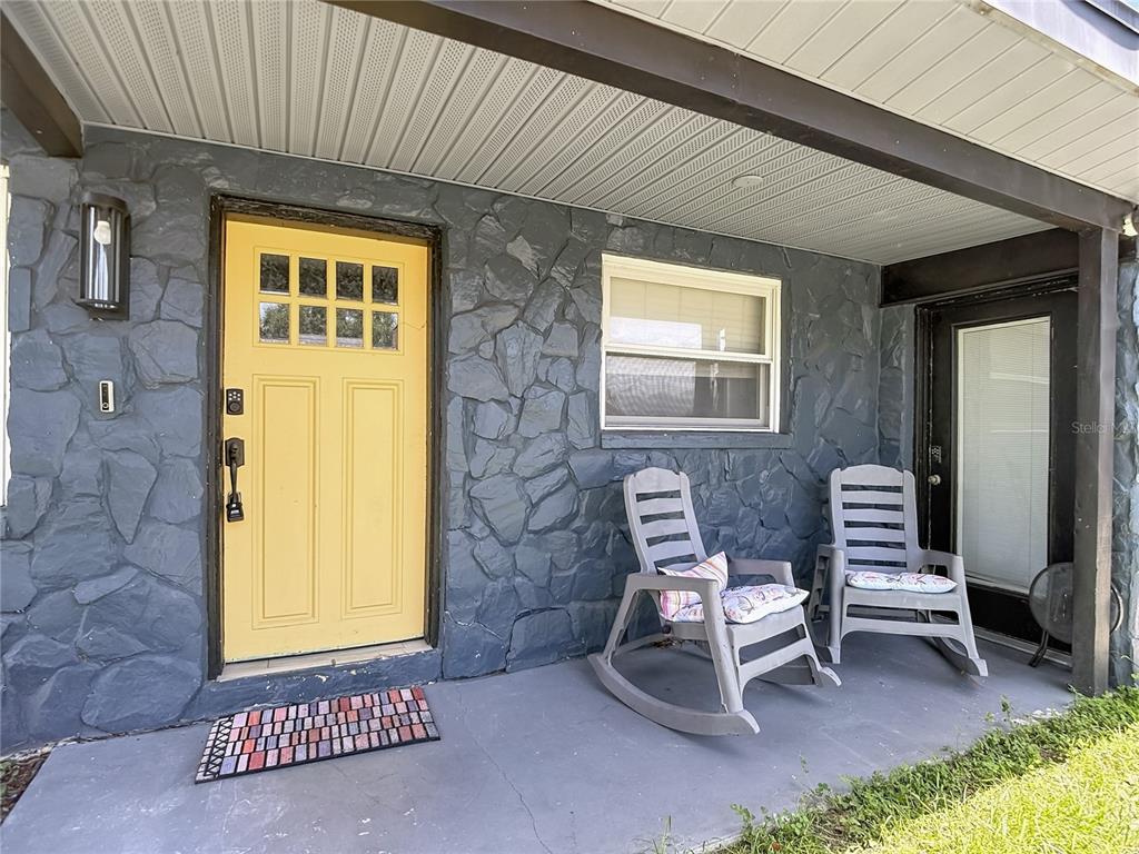 A covered porch features a yellow front door, gray stone siding, and two rocking chairs — 3313 W KATHLEEN STREET, TAMPA, FL