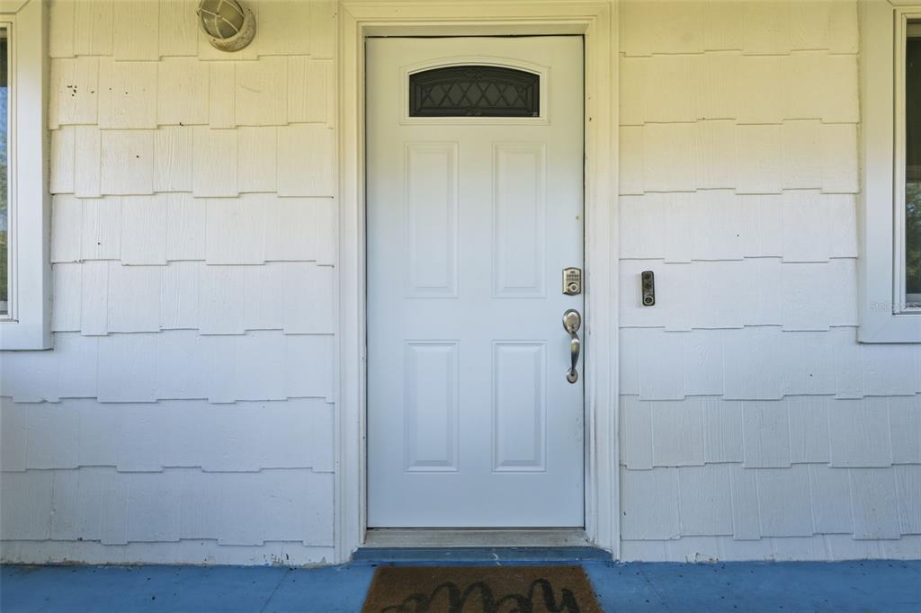 A white front door with a small window sits between white shingle siding — 10226 LYNNHAVEN ROAD, SPRING HILL, FL