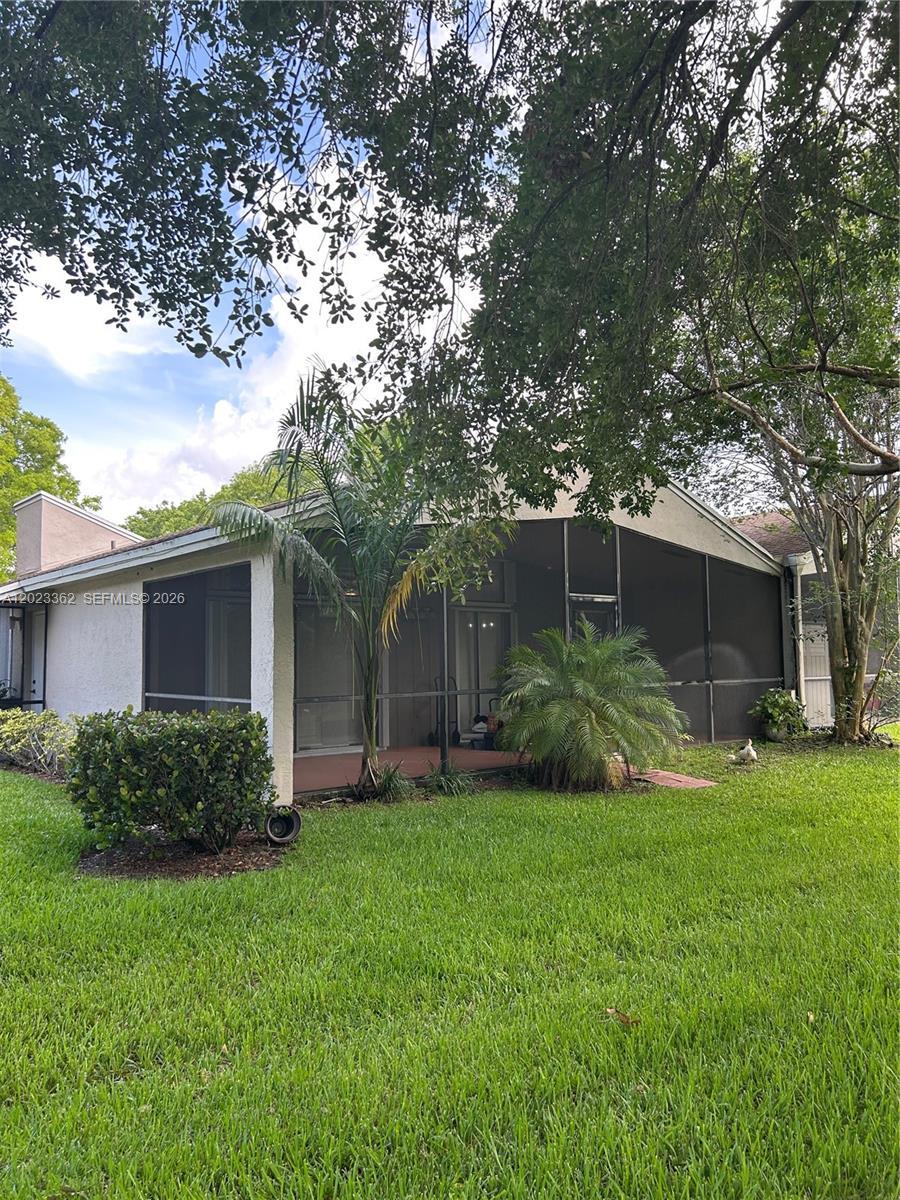 A house exterior features a screened-in patio, a grassy lawn, and mature trees — 578 Woodgate Cir, Sunrise FL 33326, SUNRISE, FL