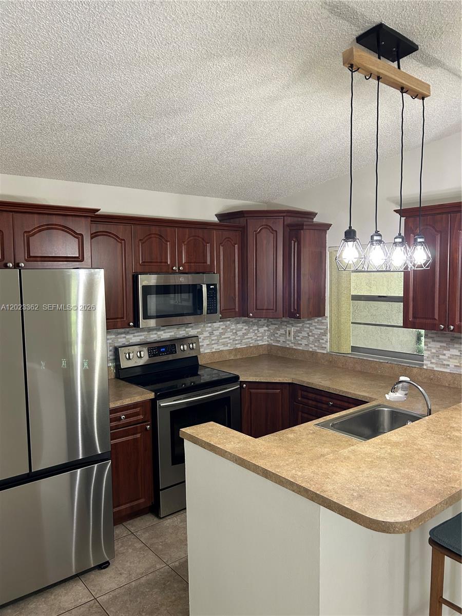 A kitchen features dark wood cabinets, stainless steel appliances, a tile backsplash, and pendant lighting — 578 Woodgate Cir, Sunrise FL 33326, SUNRISE, FL