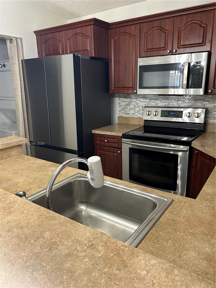 A kitchen features dark wood cabinets, stainless steel appliances, and tan laminate countertops — 578 Woodgate Cir, Sunrise FL 33326, SUNRISE, FL