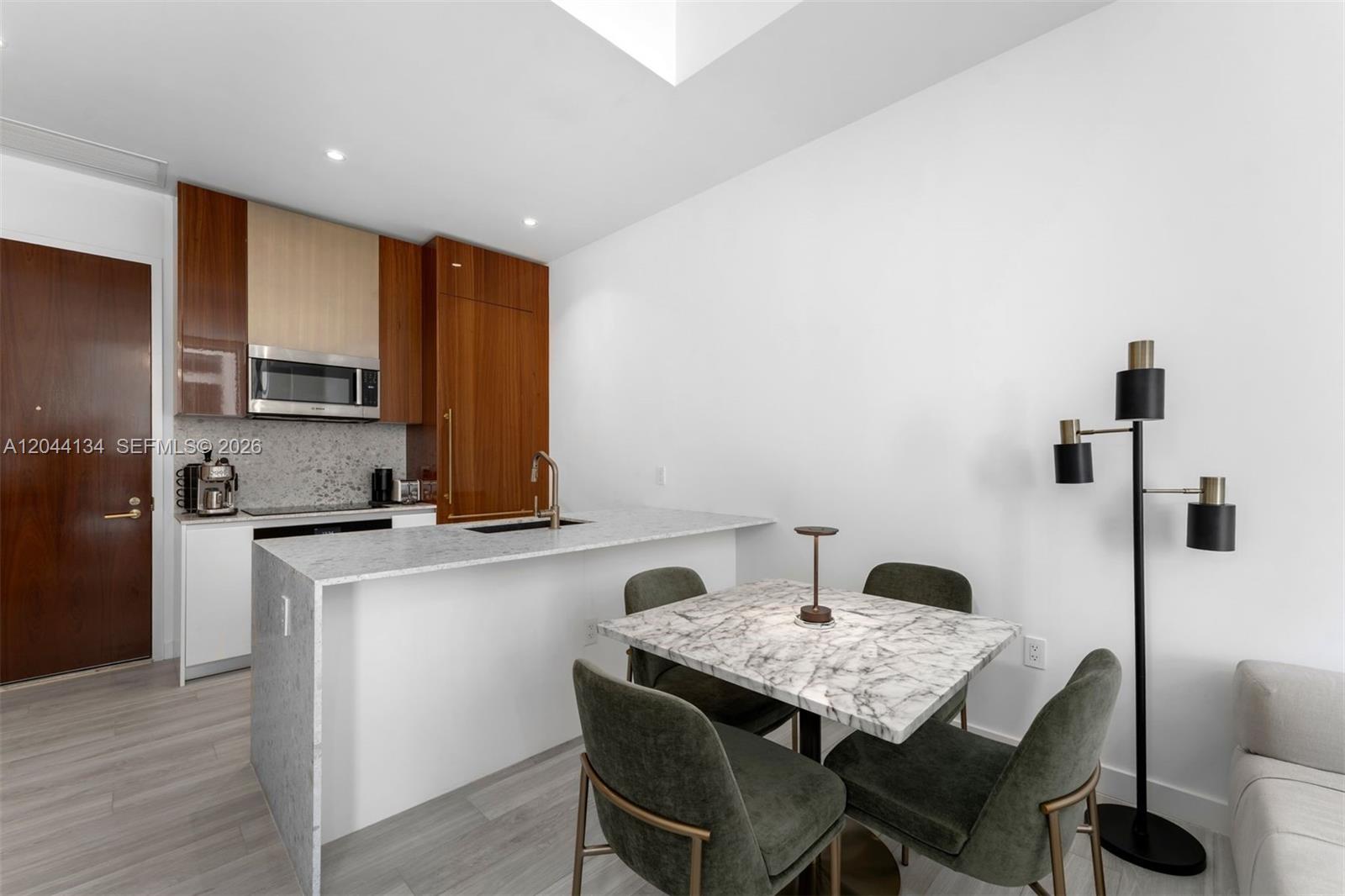A modern kitchen features wood-toned cabinetry, a marble-topped island, and an adjacent dining area — 2655 S Bayshore Dr # 908, Miami FL 33133, MIAMI, FL