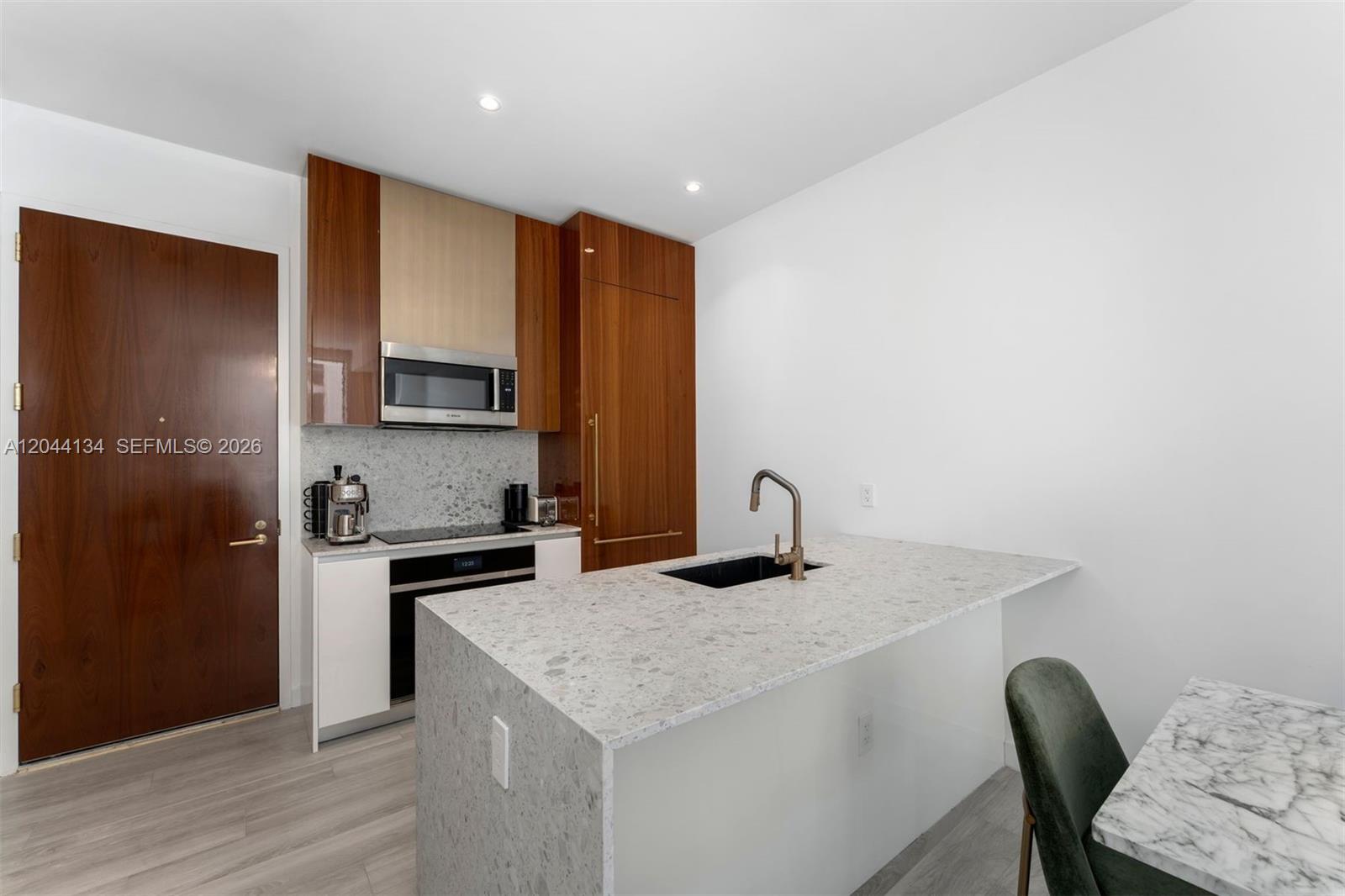 A modern kitchen features wood cabinetry, a stone island with a sink, and white walls — 2655 S Bayshore Dr # 908, Miami FL 33133, MIAMI, FL