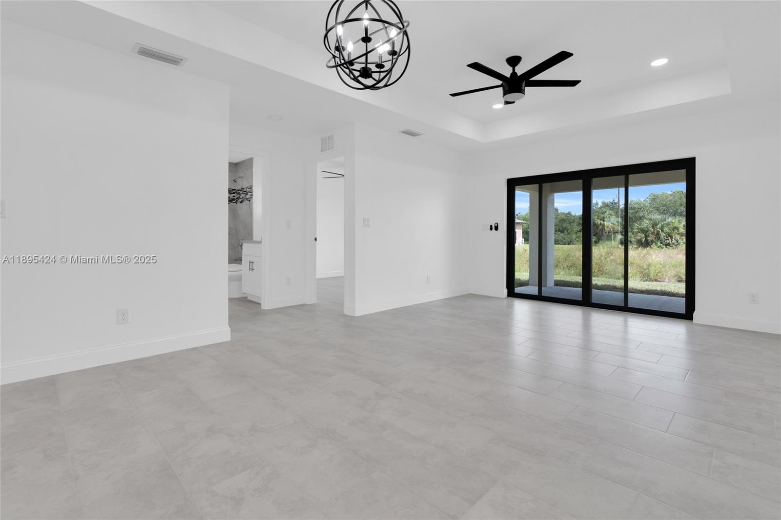 A bright, minimalist living room features gray tile flooring, a tray ceiling, and sliding glass doors — 2508 Park Rd, Lehigh Acres FL 33971, LEHIGH ACRES, FL