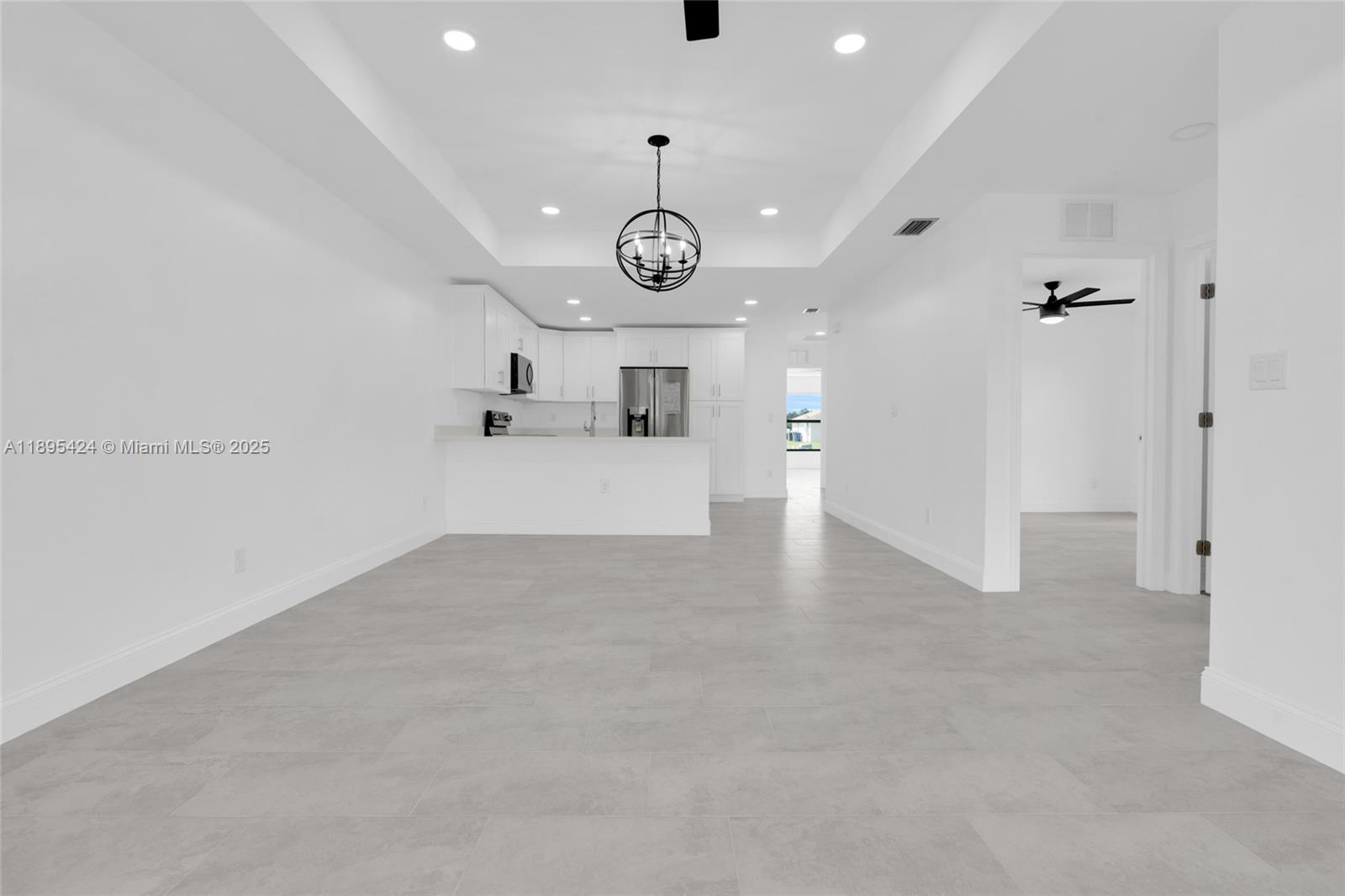 A bright, open-concept kitchen and living area features white cabinetry, tile flooring, and recessed lighting — 2508 Park Rd, Lehigh Acres FL 33971, LEHIGH ACRES, FL