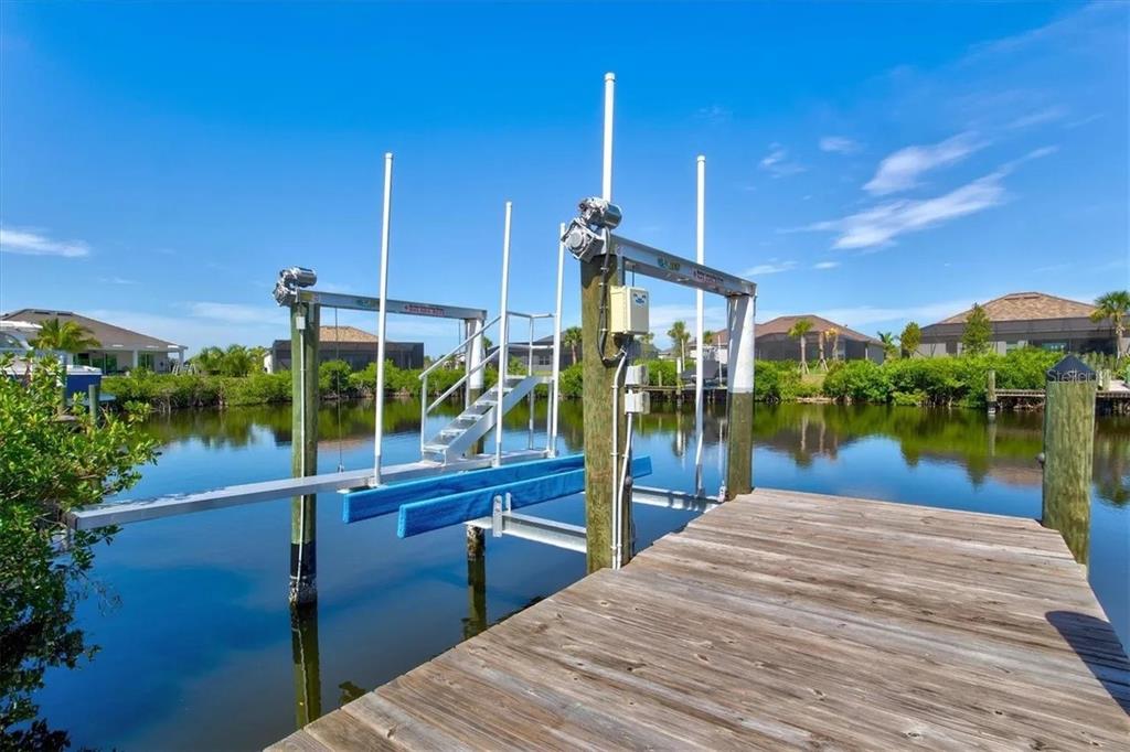 A wooden boat dock features a mechanical boat lift over a calm canal — 15024 SPANISH POINT DRIVE, PORT CHARLOTTE, FL