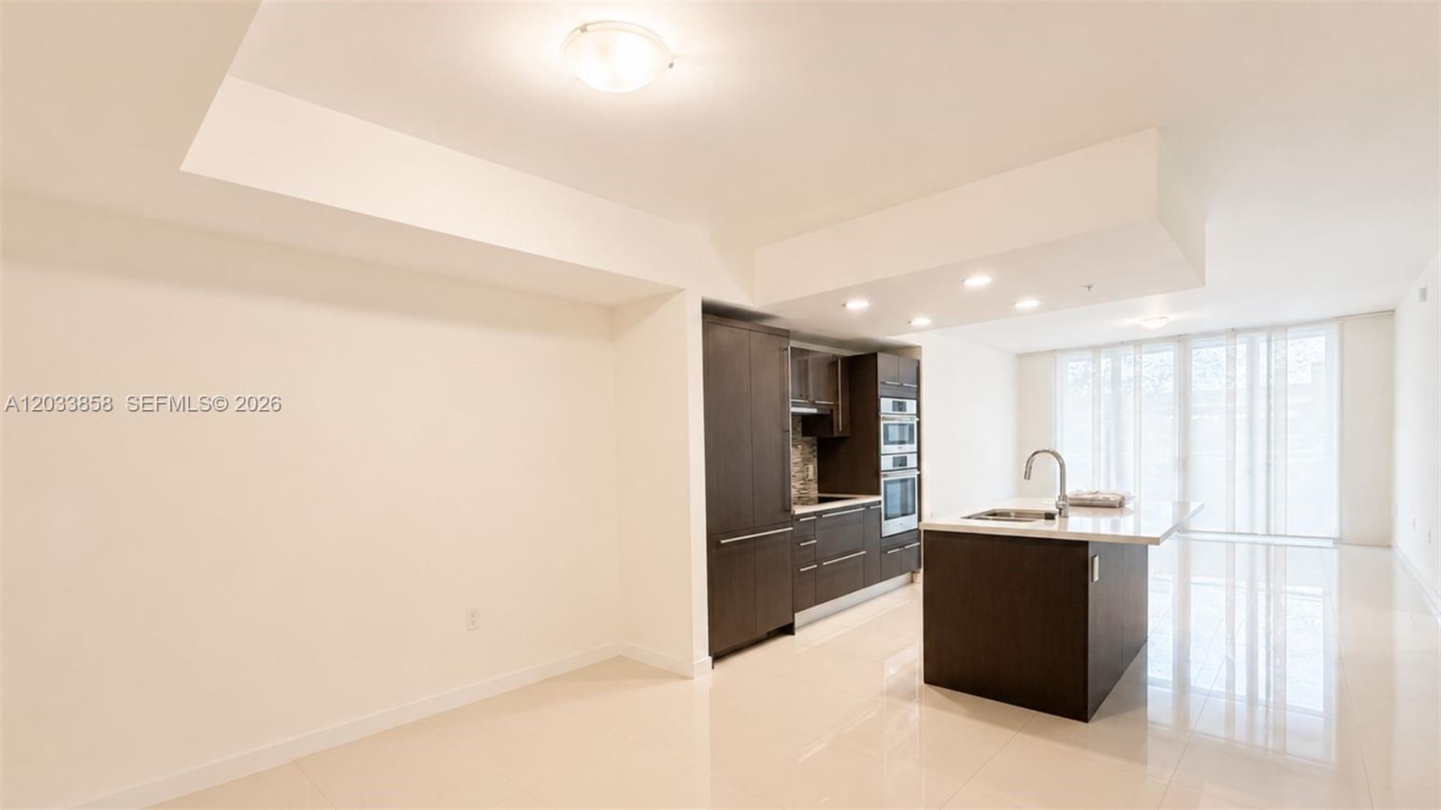 A modern kitchen features dark wood cabinetry, a white island, and light tile flooring — 7825 NW 107th Ave # 218, Doral FL 33178, DORAL, FL