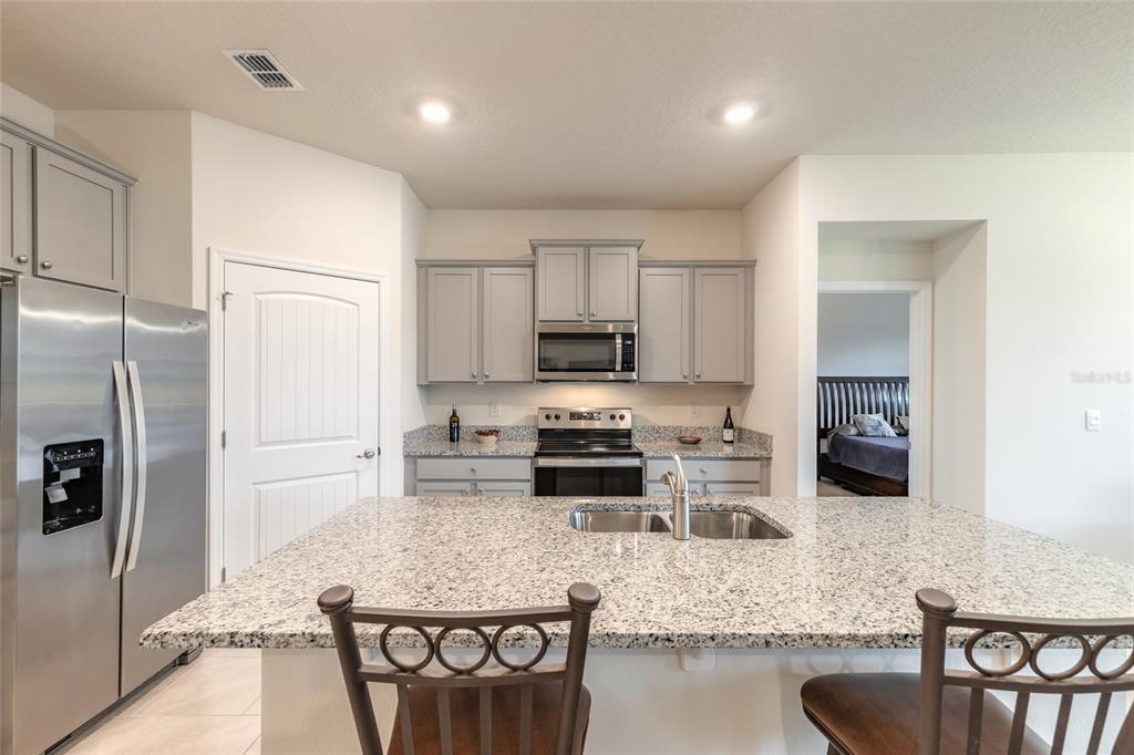 A kitchen features gray cabinets, granite countertops, a stainless steel refrigerator, and a center island — 1413 SYLES DRIVE, NEW SMYRNA BEACH, FL