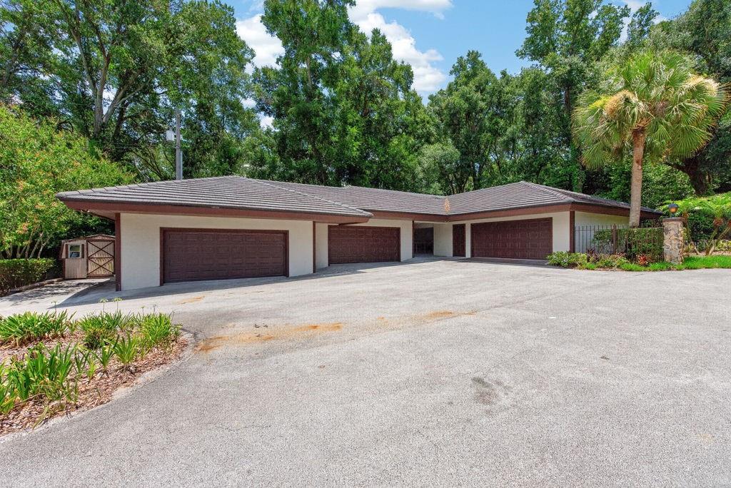 A low-slung house with three garage doors and a large asphalt driveway surrounded by trees — 1007 LAKEWOOD DRIVE, BRANDON, FL