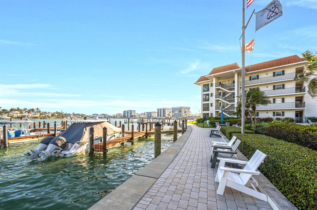 A paved walkway runs alongside a boat dock and a multi-story apartment building with balconies — 222 HARBOUR DRIVE UNIT 114, NAPLES, FL