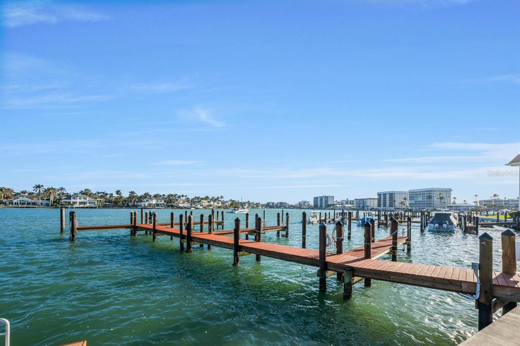 A wooden dock extends into a bay with boats and coastal buildings in the distance — 222 HARBOUR DRIVE UNIT 114, NAPLES, FL