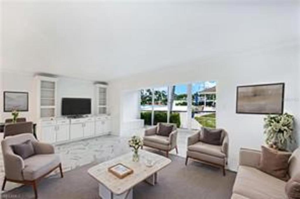 A living room with white cabinetry, a television, two armchairs, and a view of outdoors — 222 HARBOUR DRIVE UNIT 114, NAPLES, FL