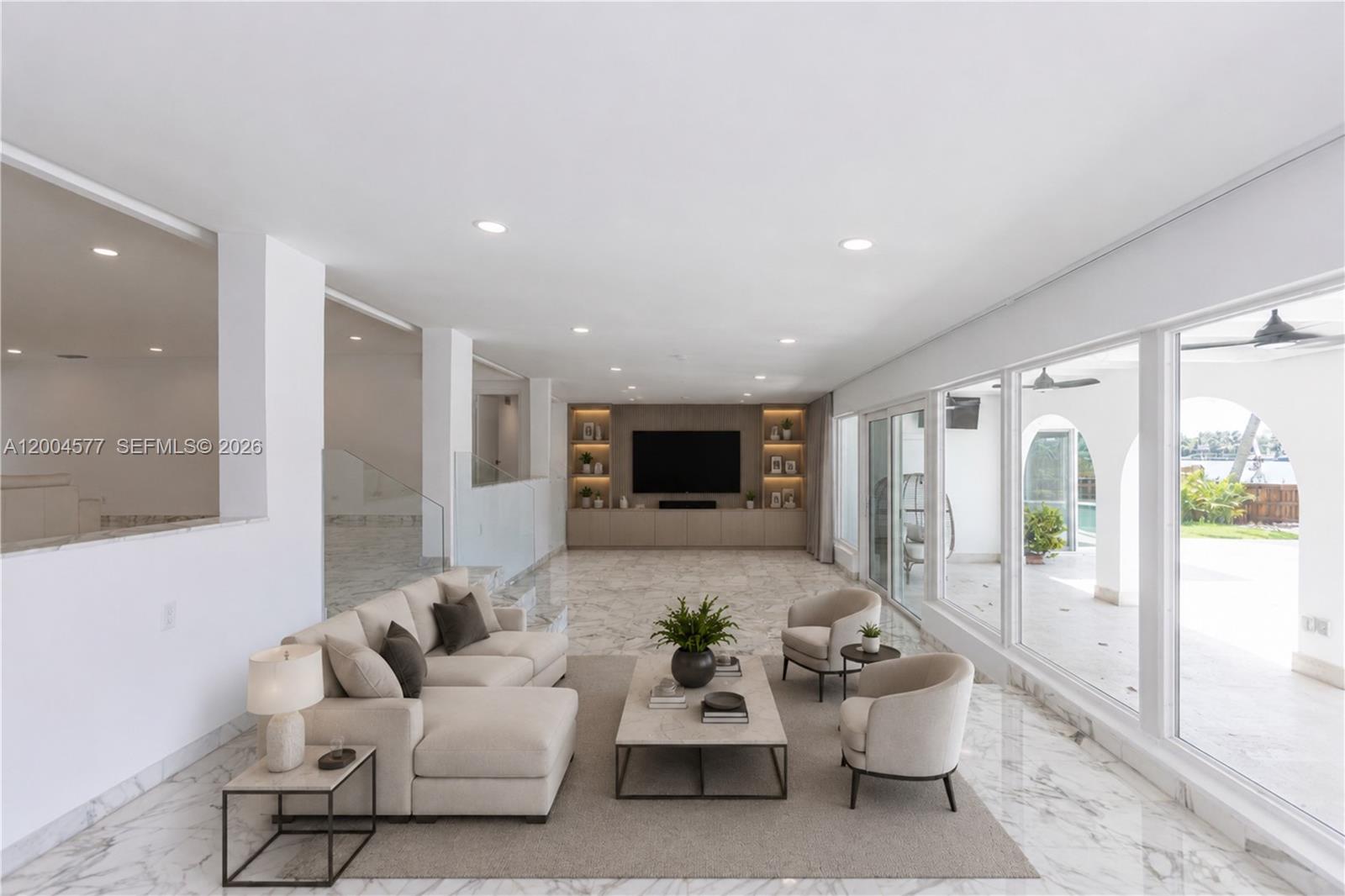 A modern living room features a sectional sofa, marble floors, and large windows overlooking water — 1690 Daytonia Rd, Miami Beach FL 33141, MIAMI BEACH, FL