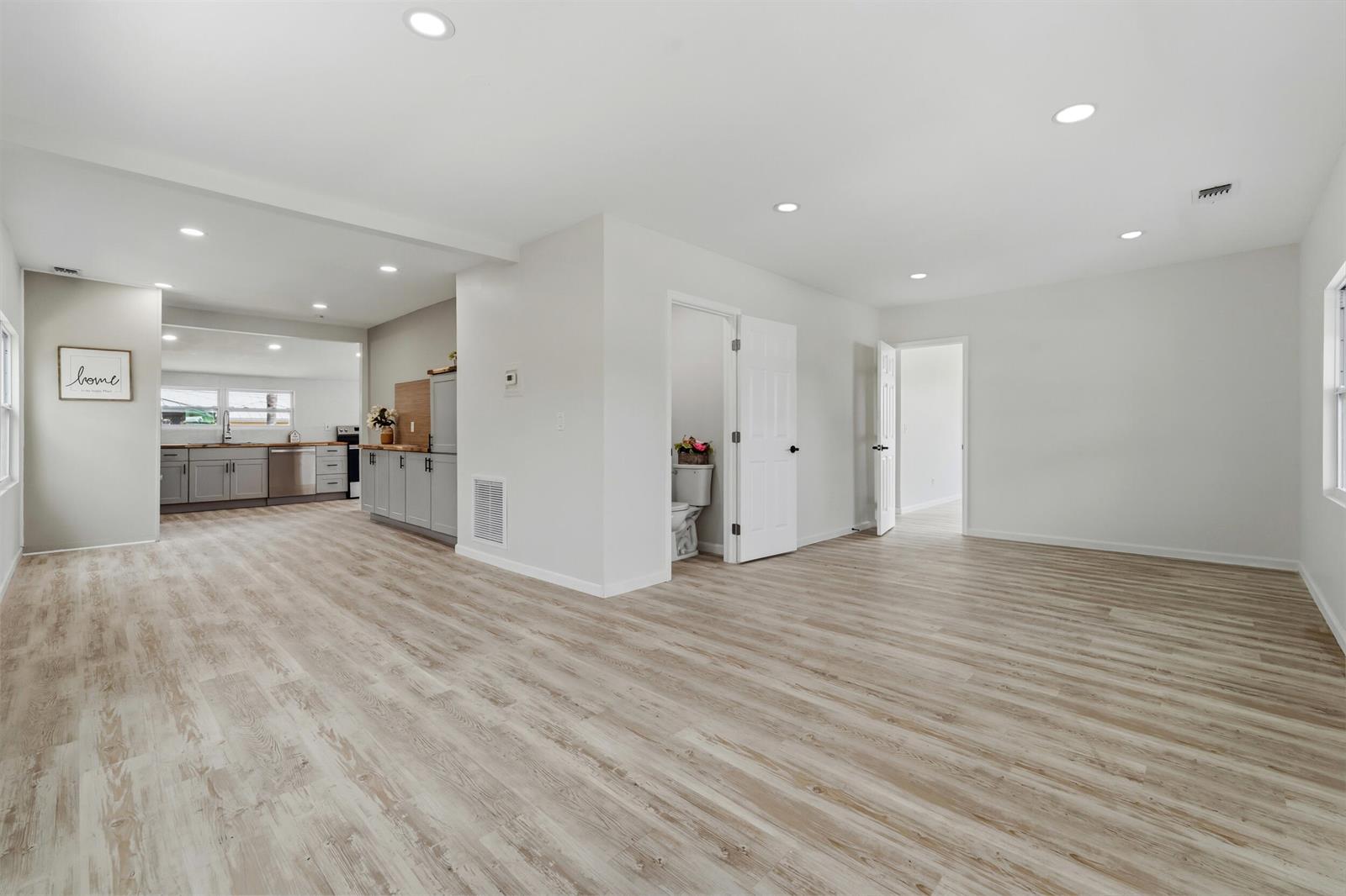 An open-concept living area features light wood-look flooring, recessed lighting, and an adjacent kitchen — 1566 NW 9th Avenue, Stuart FL 34994, STUART, FL