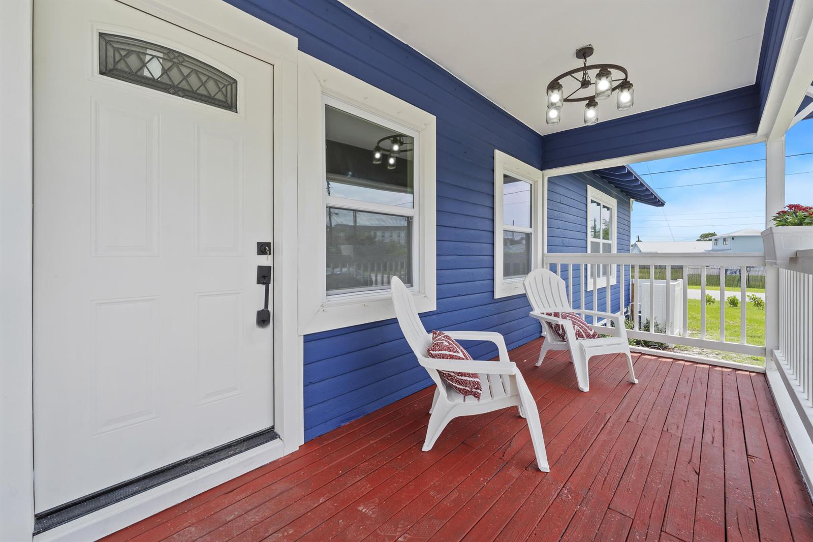 A blue-sided porch features a red wooden deck, white chairs, and a hanging light fixture — 1566 NW 9th Avenue, Stuart FL 34994, STUART, FL